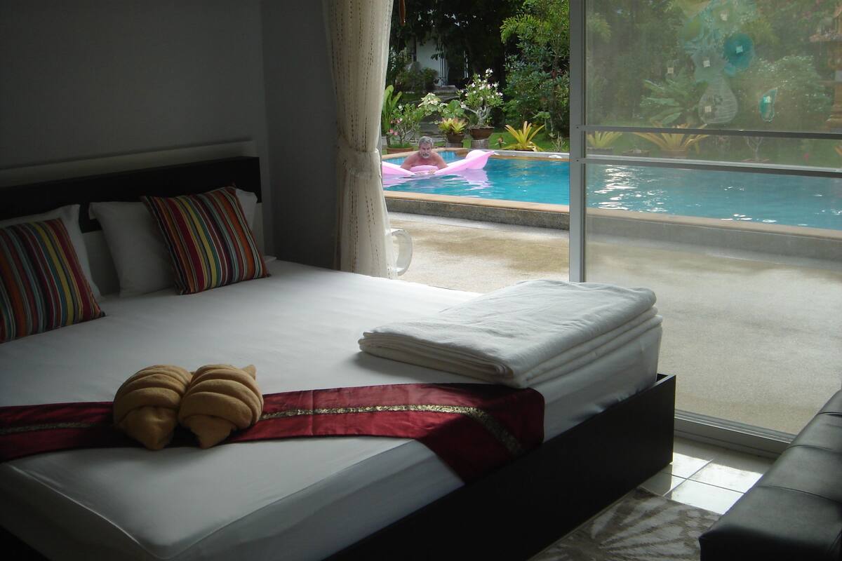 A hotel room with a large bed, a view of a swimming pool, and a balcony.