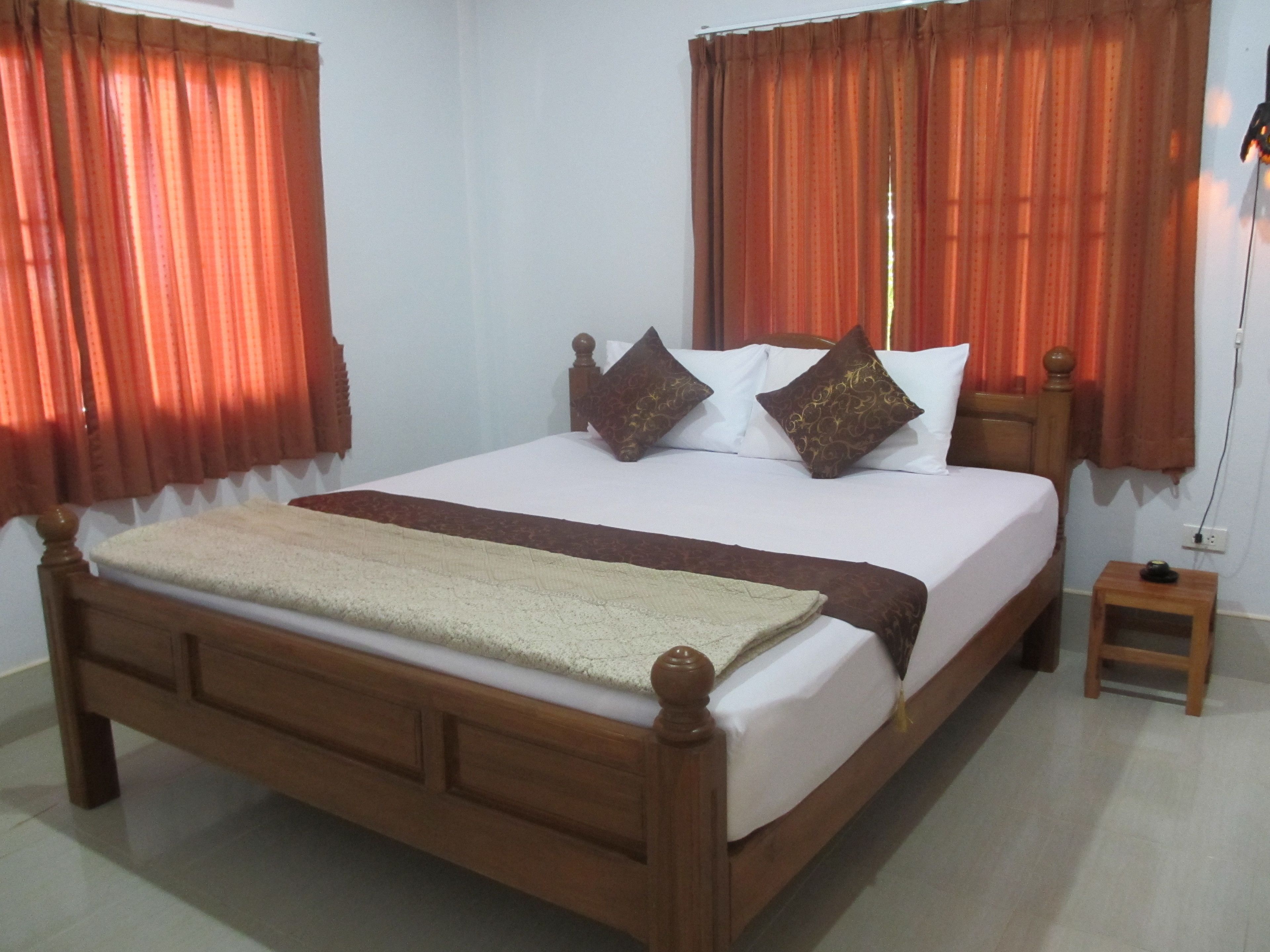 Una cama bien tendida con estructura de madera, ropa de cama blanca y almohadas decorativas. Junto a la cama hay una mesita de noche de madera con una lámpara.