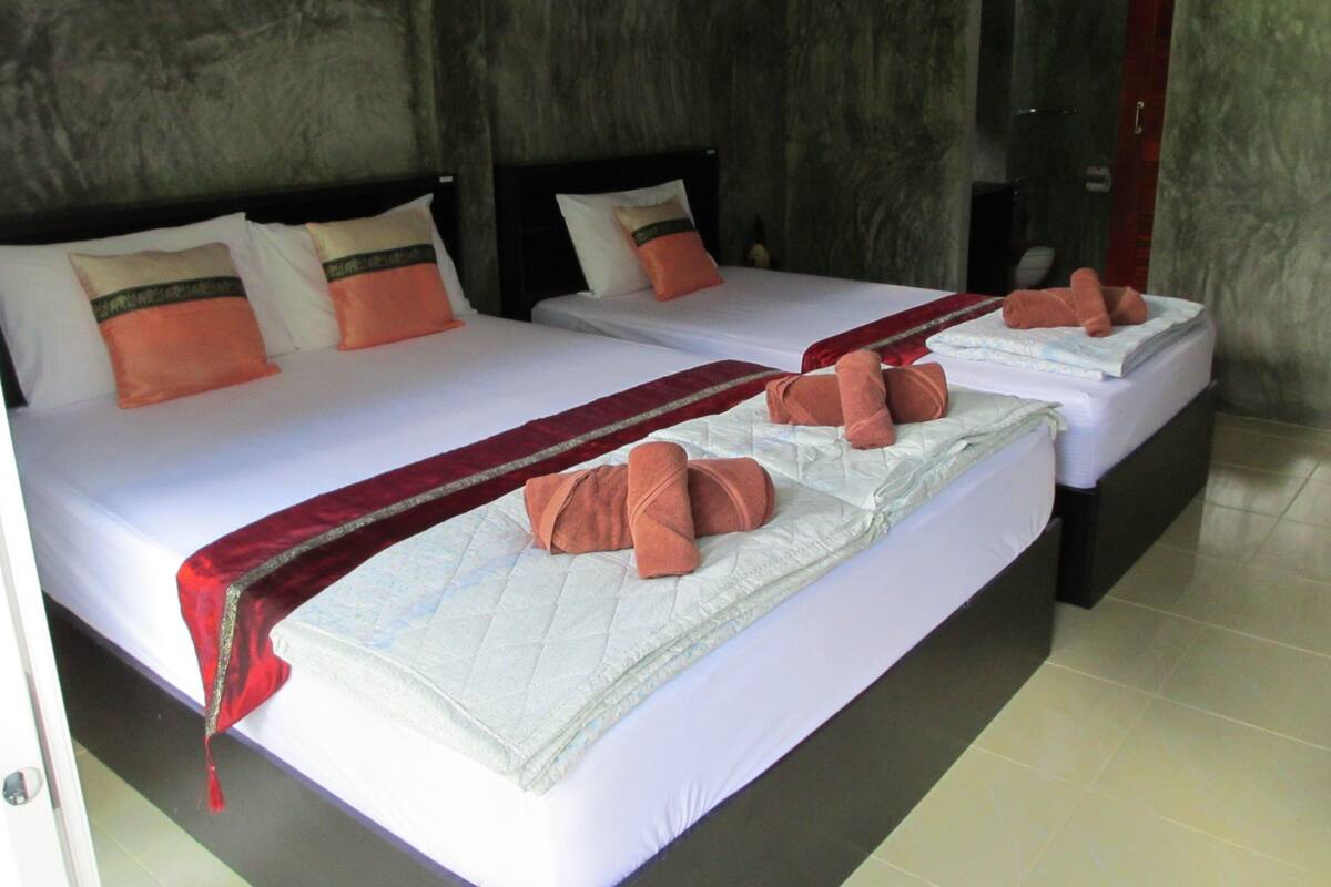 A hotel room with two beds, each with white linens, orange pillows, and red bedspreads.