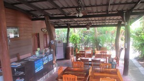 A covered outdoor dining area with wooden tables and chairs, a refrigerator, and a counter with various items. - Real Relax Resort & Beauty Massage (Krabi)