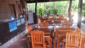 A covered outdoor dining area with wooden tables and chairs, a counter with a computer, and a view of lush greenery. - Real Relax Resort & Beauty Massage (Krabi)