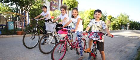 Un grupo de niños en bicicleta en un entorno al aire libre, con edificios y árboles de fondo.