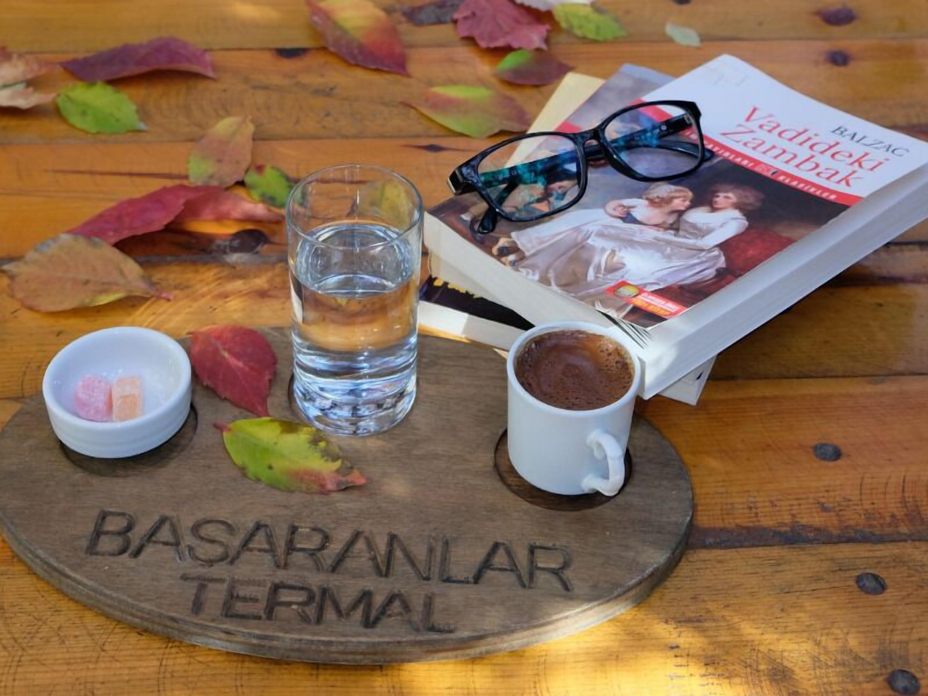 Ein Holztisch mit einem Glas Wasser, einer Kaffeetasse, einem Buch und einer Brille.