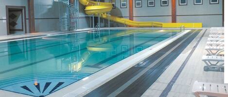 A large indoor swimming pool with a yellow water slide and a diving platform.