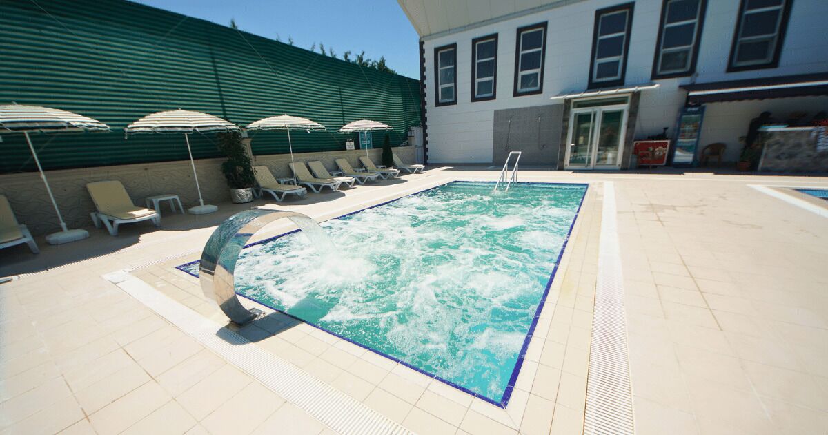 Ein Pool mit Liegestühlen und Sonnenschirmen, umgeben von einem Gebäude mit einer grünen Wand und Fenstern.