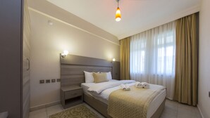 Habitación de hotel con una cama grande, una mesita de noche y una alfombra estampada, además de un ventanal con cortinas.