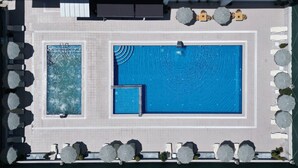 Vista aérea de un área de piscina de hotel con dos piscinas, tumbonas y sombrillas.