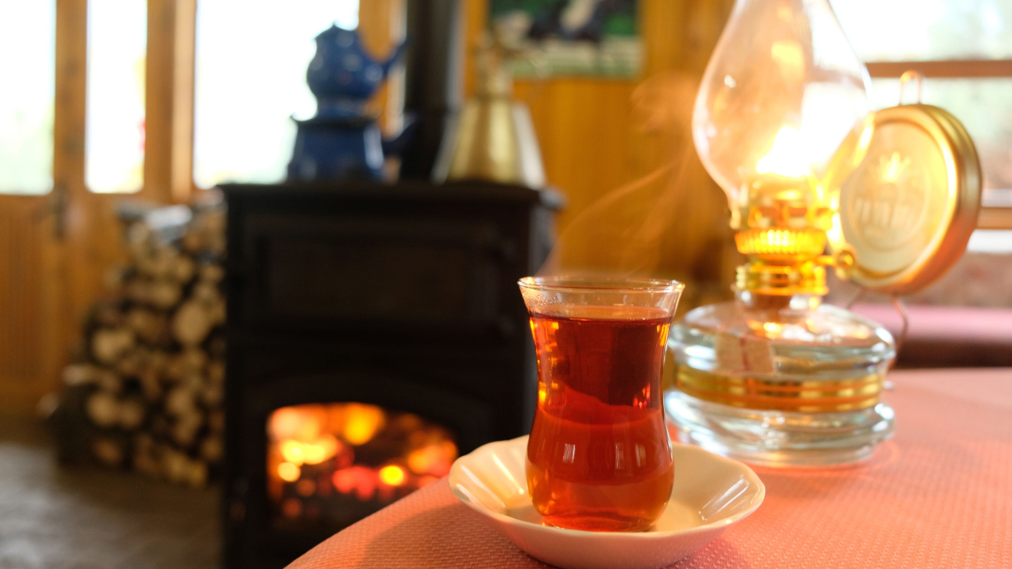 Una taza de té sobre un platillo, una vela encendida y una lámpara decorativa.