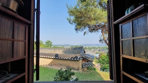 Una porta in legno aperta che mostra un edificio tradizionale coreano con tetti a tegole e vista su un albero e un paesaggio lontano.