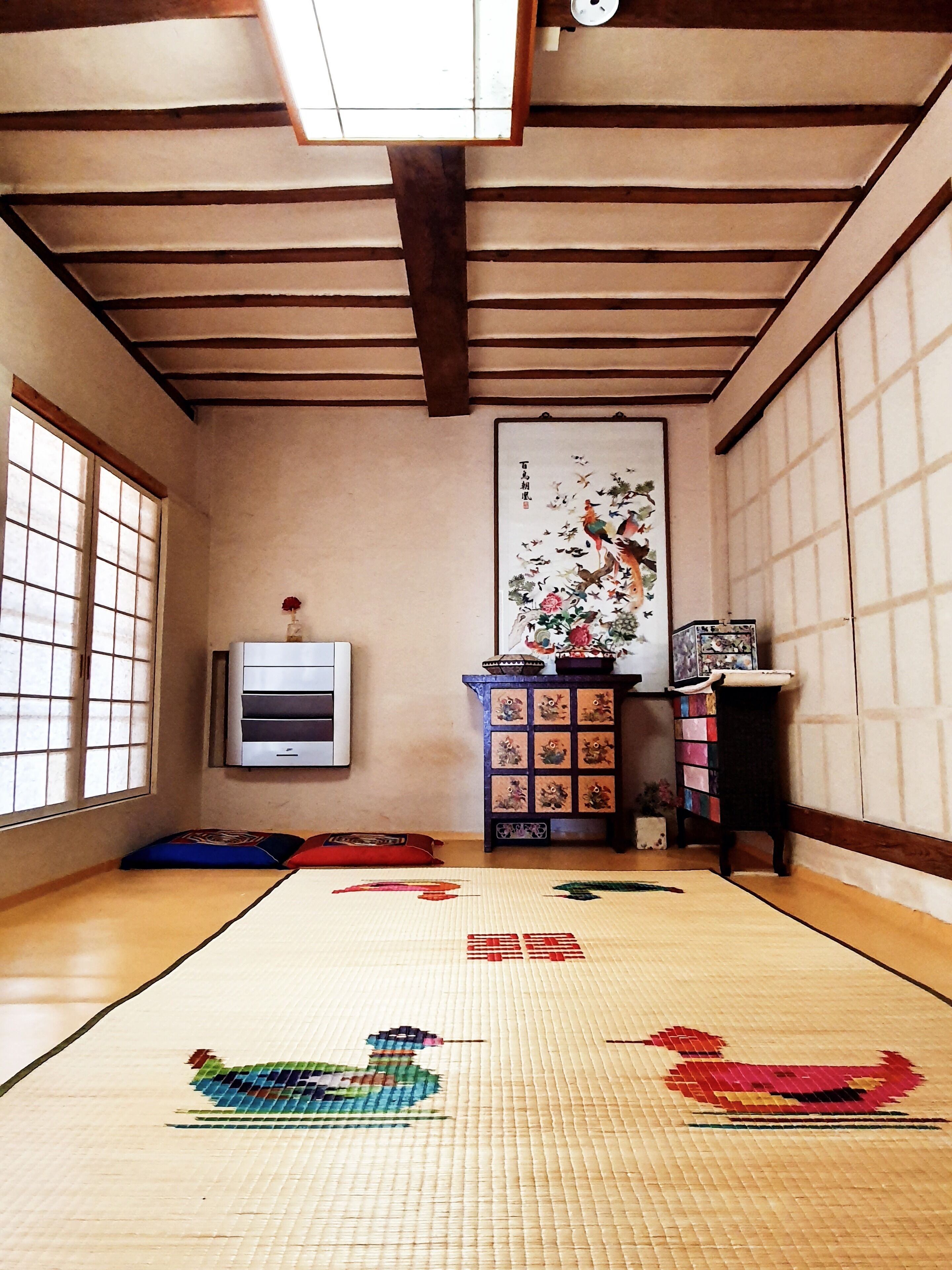 Una stanza con pavimento in tatami, un paravento shoji, tappeti in tatami, un dipinto tradizionale giapponese e un piccolo mobile con oggetti decorativi.