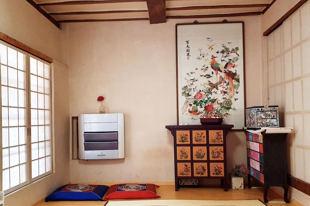A traditional Japanese room with tatami flooring, a shoji screen, a mounted air conditioner, a decorative cabinet with floral carvings, and a framed artwork on the wall.