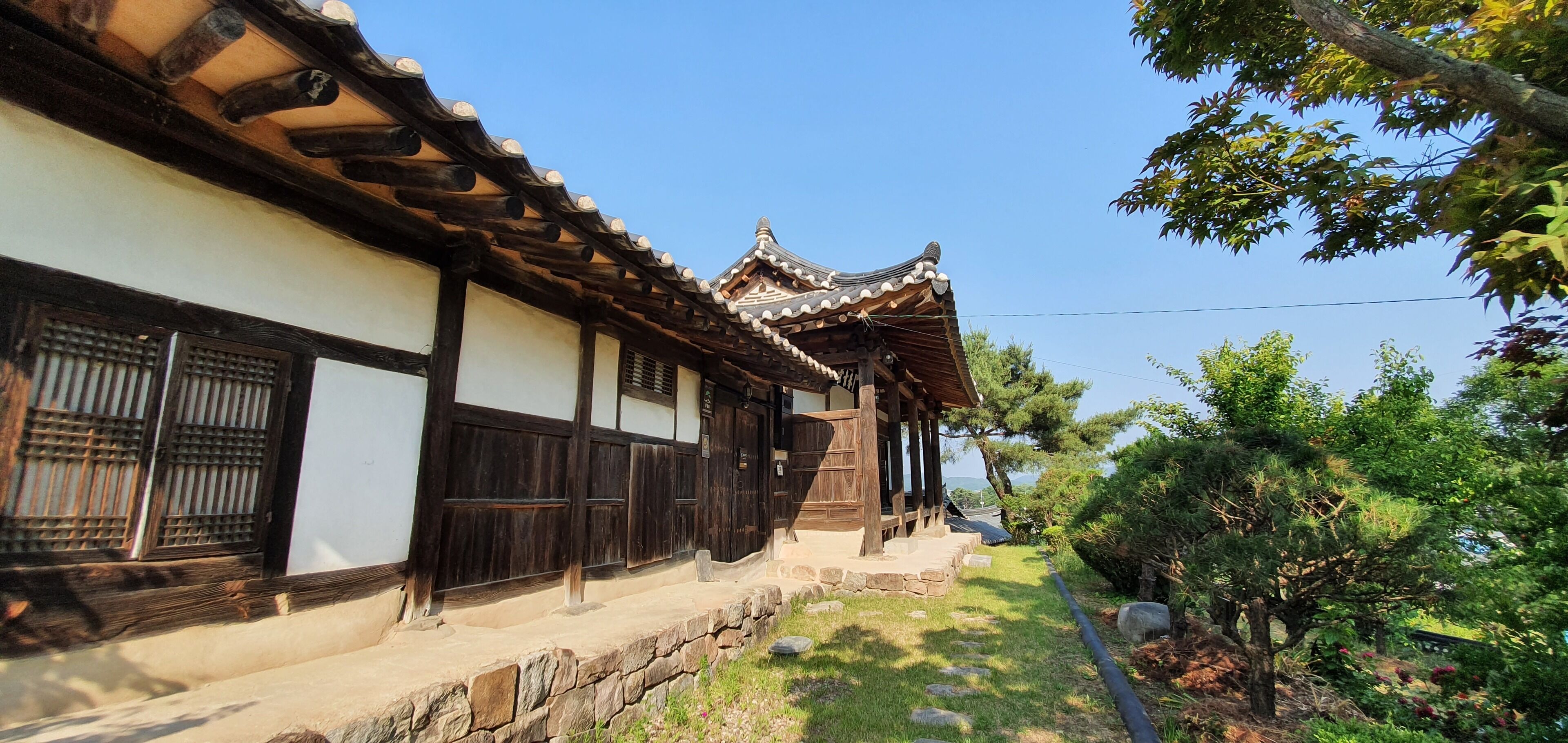 A traditional building with wooden beams and tiled roofs, surrounded by greenery and a clear sky.