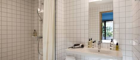 Un baño con ducha, lavamanos con artículos de aseo y espejo.