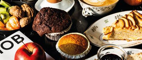 Una mesa con diversos alimentos, incluyendo un muffin, una porción de pastel, una taza de café y un bol de fruta.
