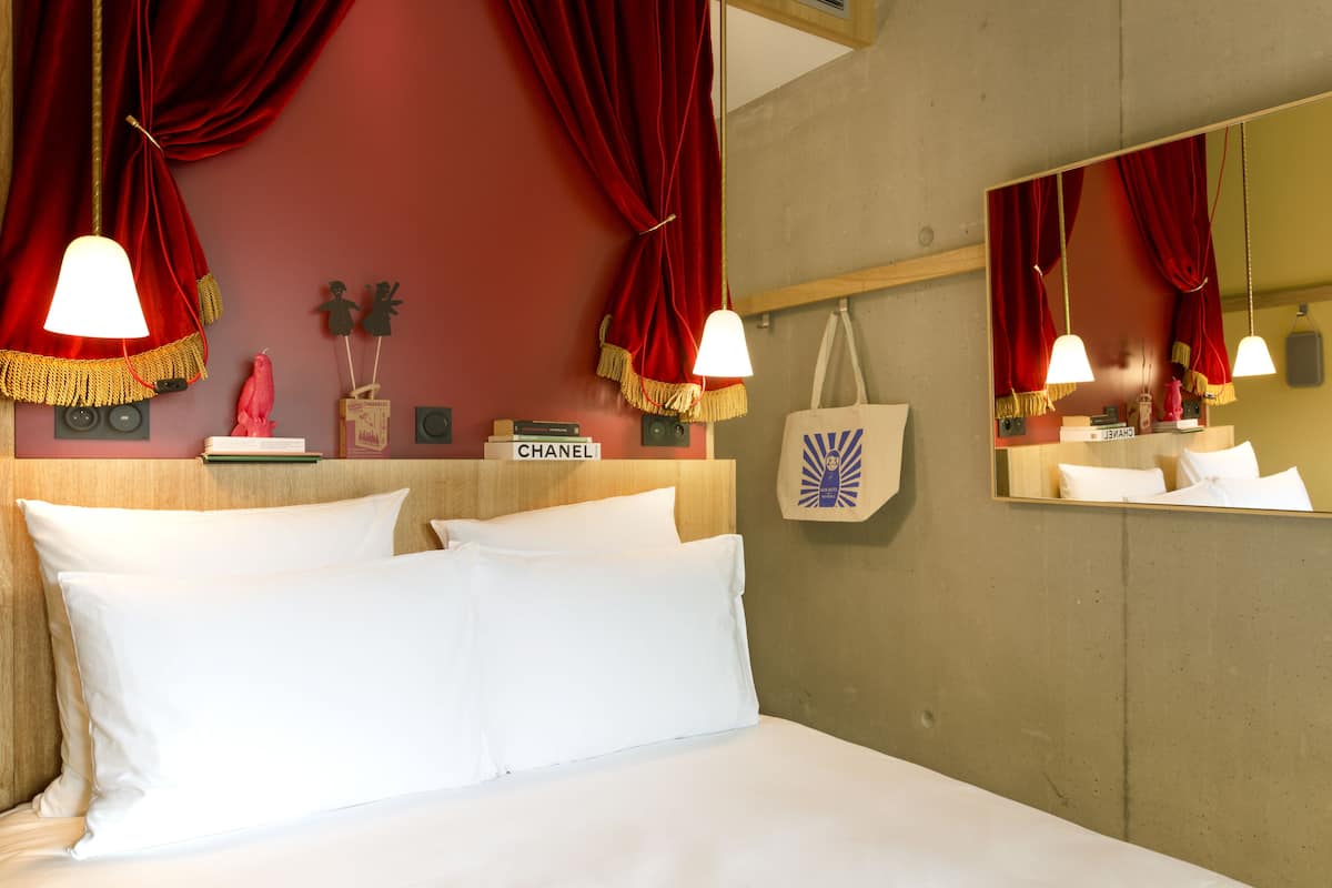 Une chambre d’hôtel avec un lit, des rideaux rouges, un miroir et un panneau publicitaire Chanel.