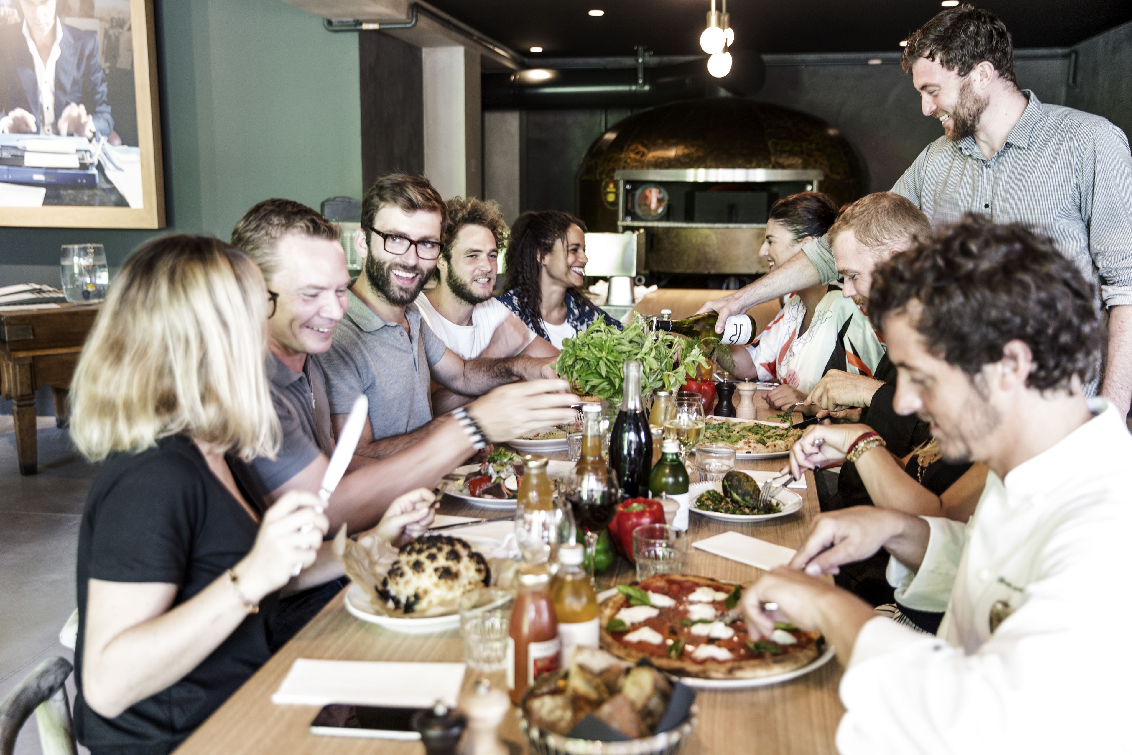Un grupo de personas cenando en un restaurante, con pizza y varios platos en la mesa.
