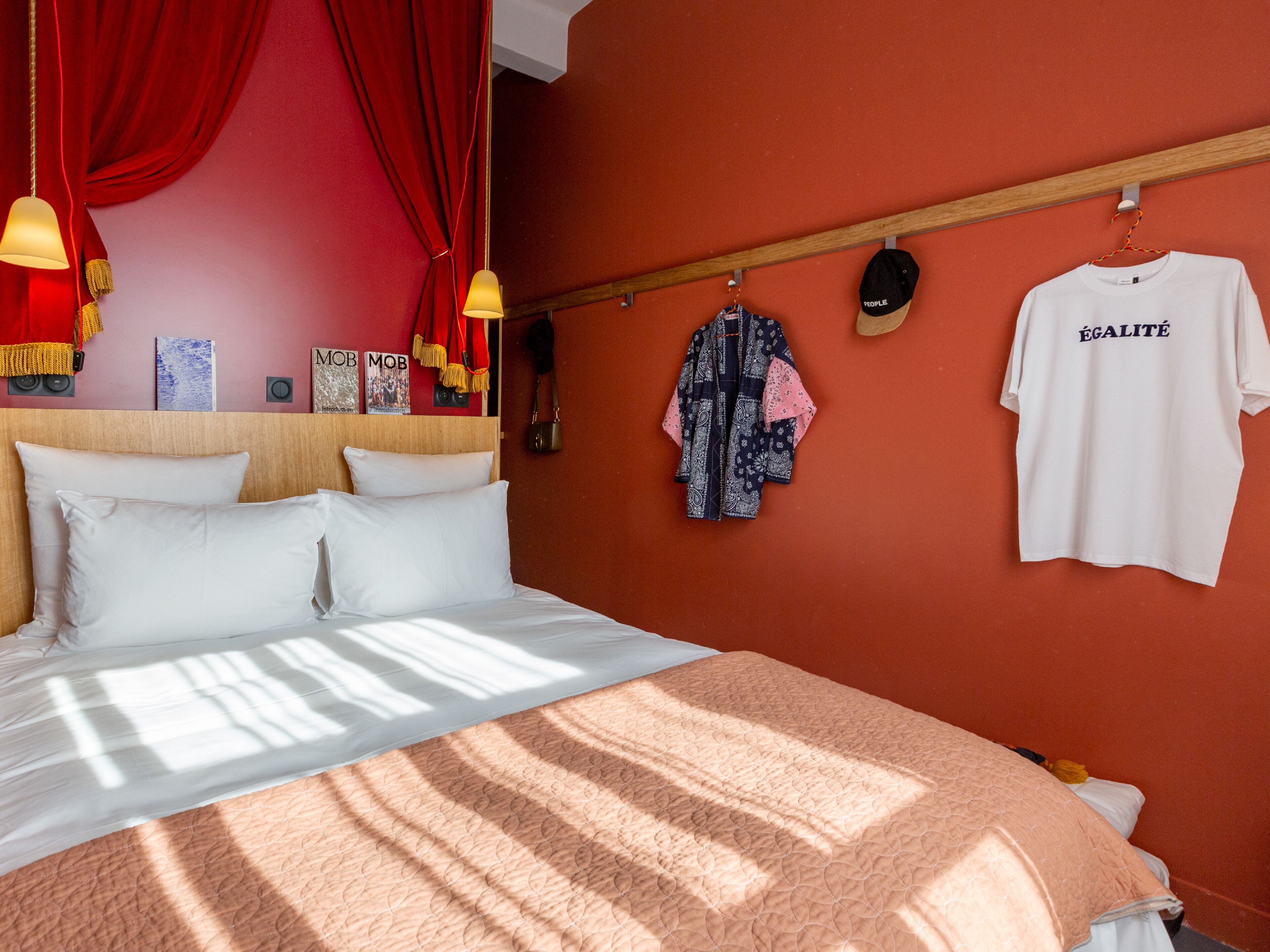 A neatly made bed with white linens, a red wall, and a wooden headboard.