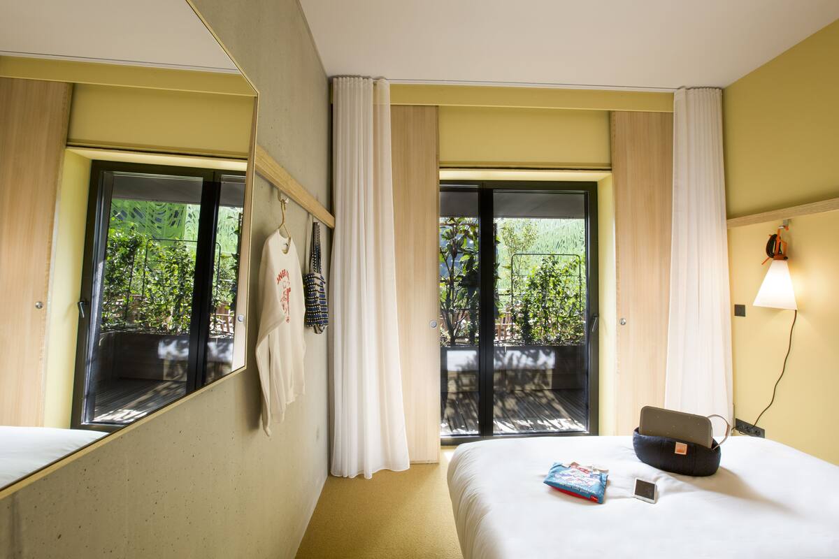 Une chambre d’hôtel avec un lit, une table de chevet, une lampe et une fenêtre avec des rideaux.