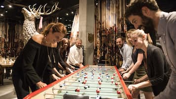 Un grupo de personas jugando al fútbol de mesa en una habitación con una gran cabeza de alce decorativa y una pared de fotografías enmarcadas.