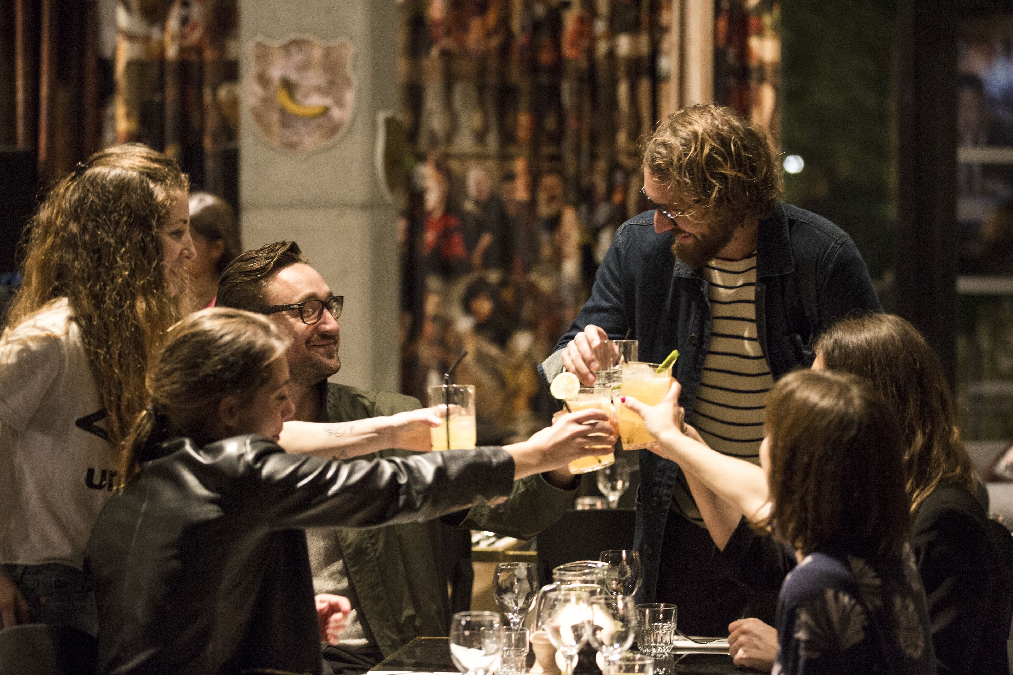Un groupe de personnes trinquant avec des boissons autour d’une table dans un restaurant.