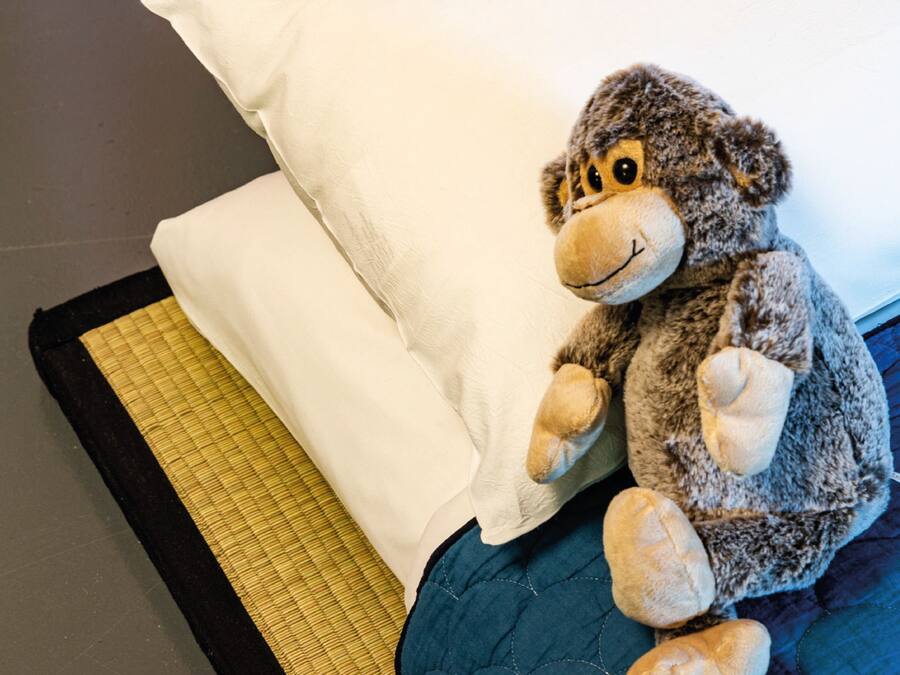 Un jouet en peluche sur un lit, avec un oreiller blanc et une couverture rayée jaune et noire.