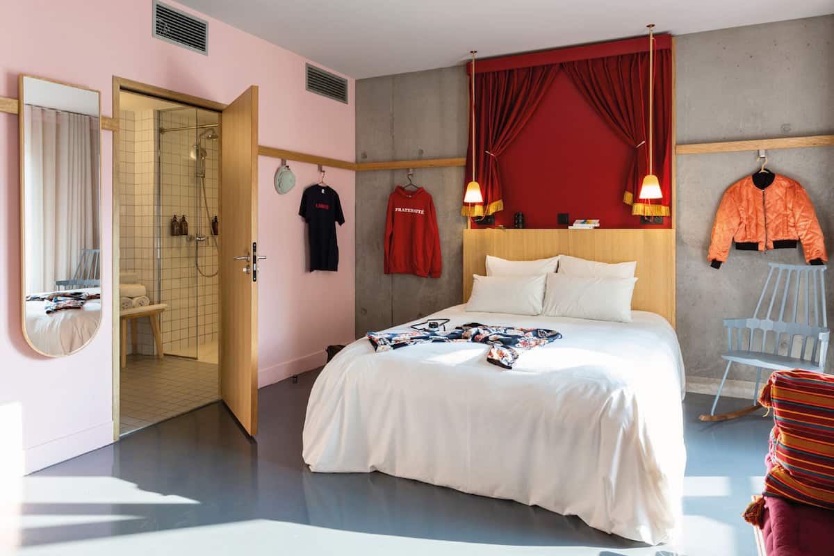 Une chambre à coucher avec un grand lit, une tête de lit en bois, un rideau rouge et une veste suspendue.