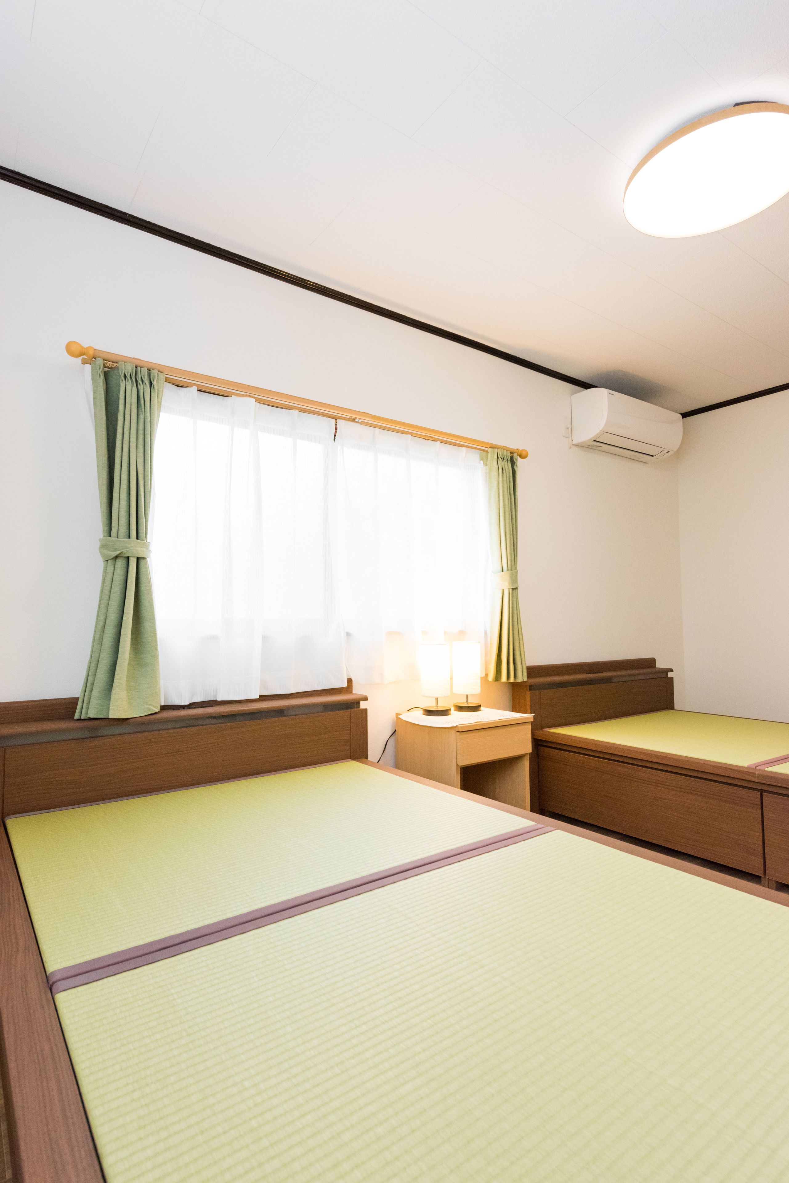 A room with two beds, a desk, a lamp, and a window with curtains.