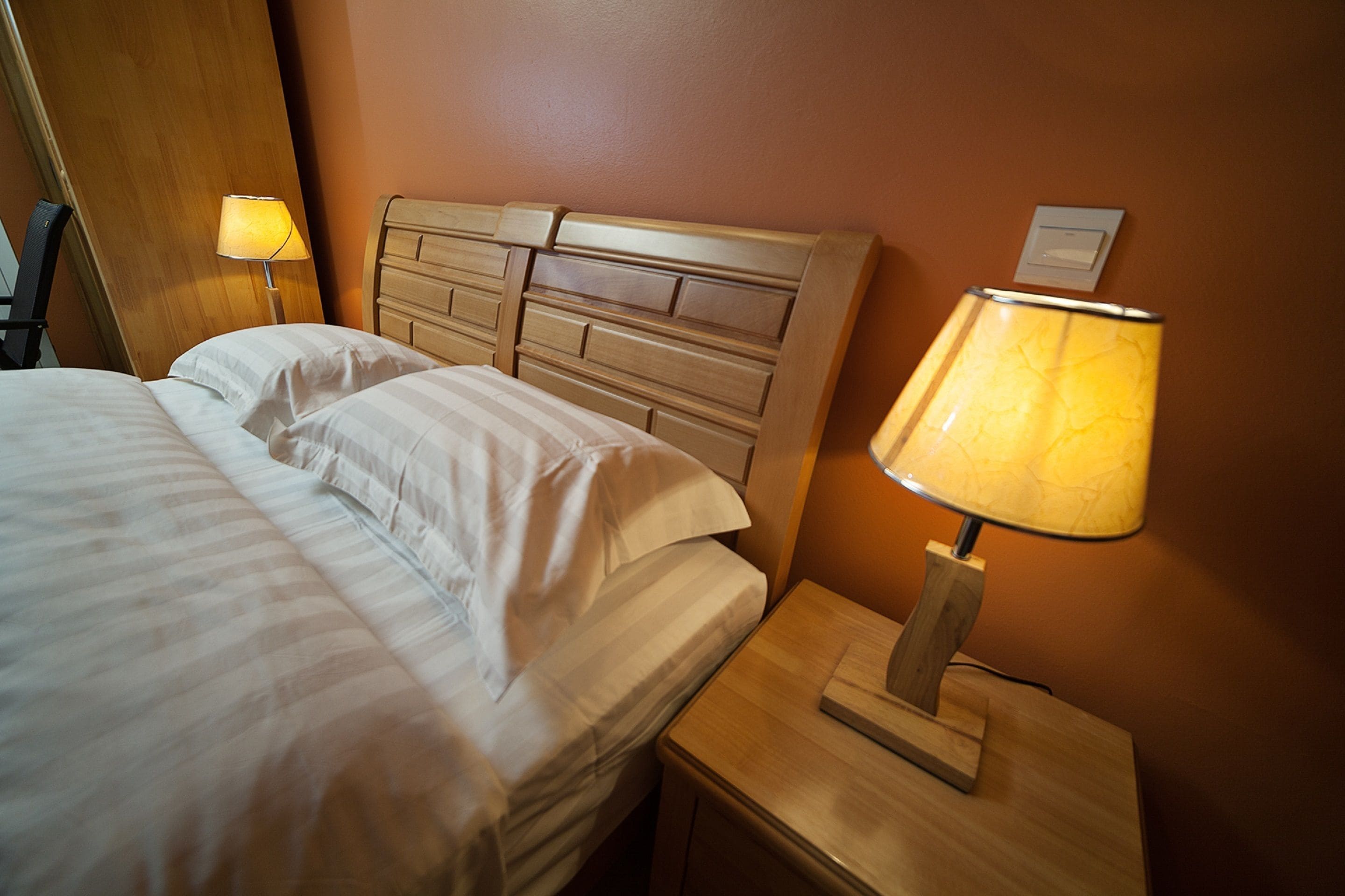 A neatly made bed with white linens, a wooden headboard, and a bedside table with a lamp.