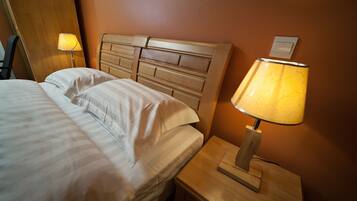 A neatly made bed with white linens, a wooden headboard, and a bedside table with a lamp.
