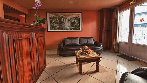 Un hall d’hôtel avec un comptoir d’accueil en bois, un canapé en cuir noir, une table basse agrémentée d’un arrangement floral et un tableau encadré représentant une cascade.