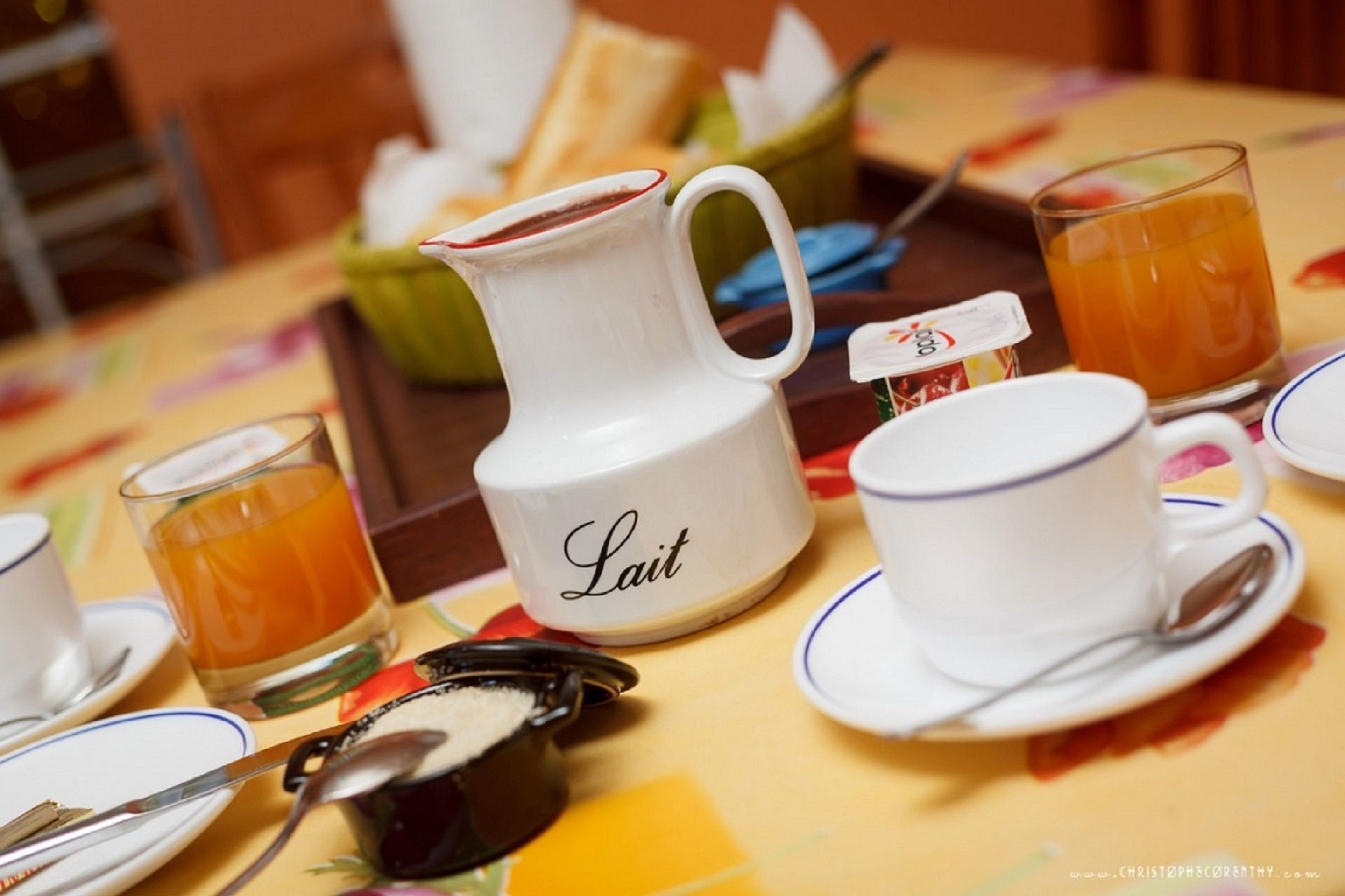 A breakfast setting with a pitcher labeled "Lait," a cup and saucer, a glass of orange juice, and a bowl of food.