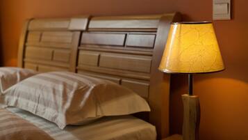 A bed with striped bedding and a wooden headboard, a bedside table with a lamp, and a wall switch.