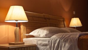 Un lit bien fait, avec du linge de lit blanc, une table de chevet en bois surmontée d’une lampe et une tête de lit.