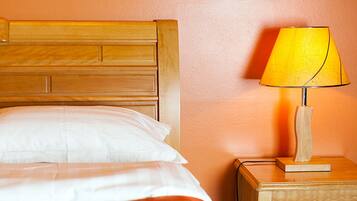 A neatly made bed with white linens and a wooden headboard, a bedside table with a lamp, and a plain orange wall.