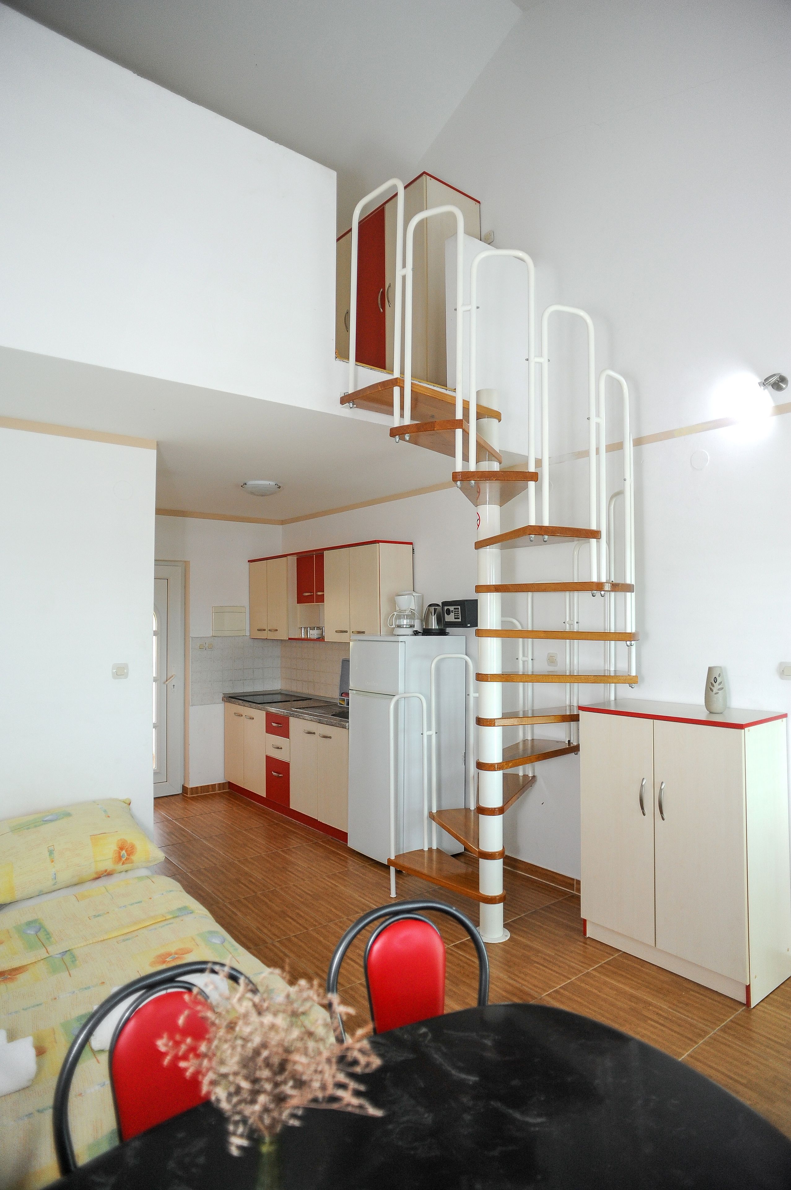 A compact kitchen with white cabinets, a red-framed upper cabinet, and a white refrigerator.