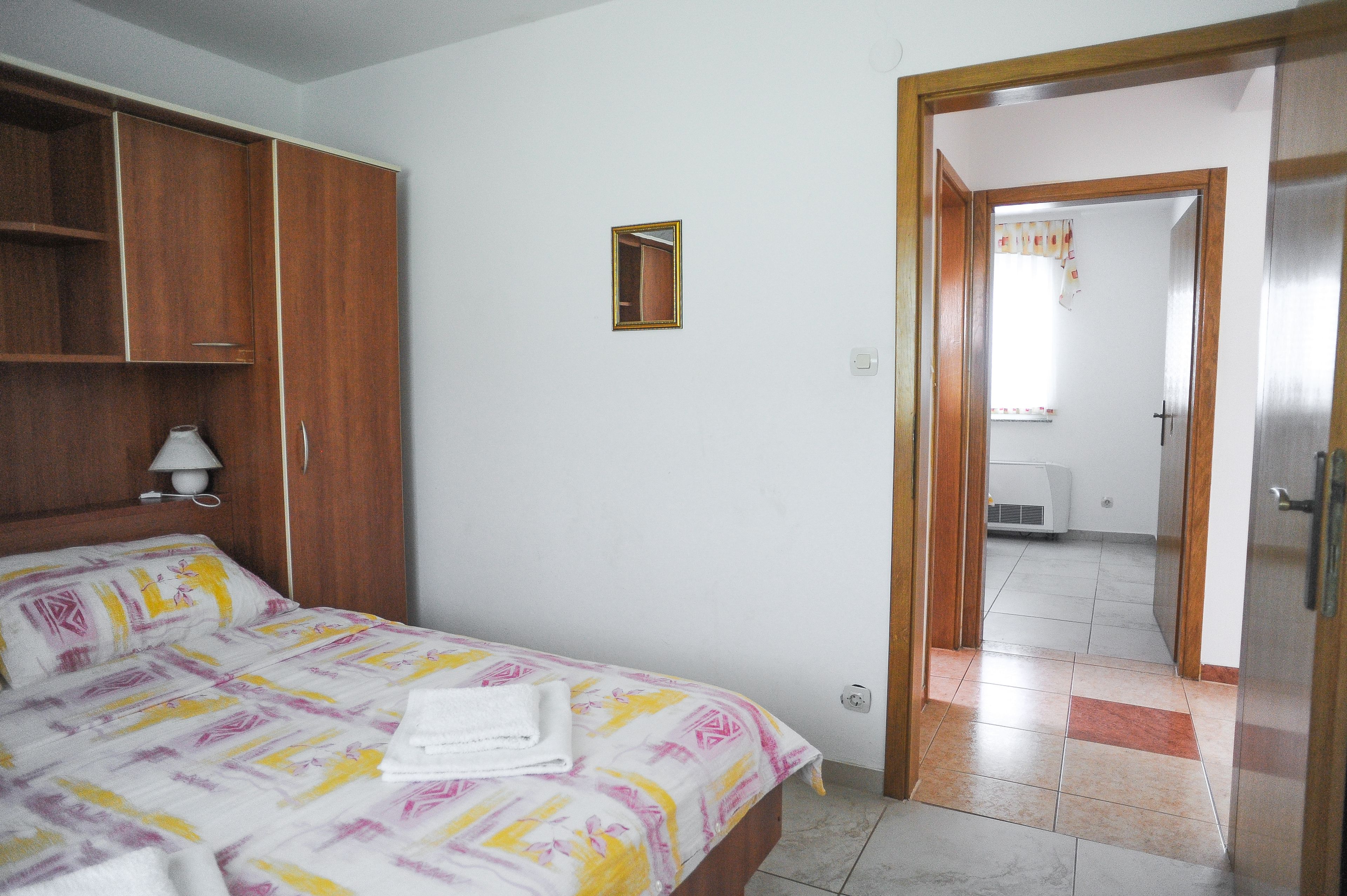 Une chambre d’hôtel avec un lit, une armoire en bois, un petit miroir et une porte donnant sur une salle de bain.
