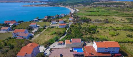 An aerial view of a coastal village with houses, a swimming pool, and a beach.