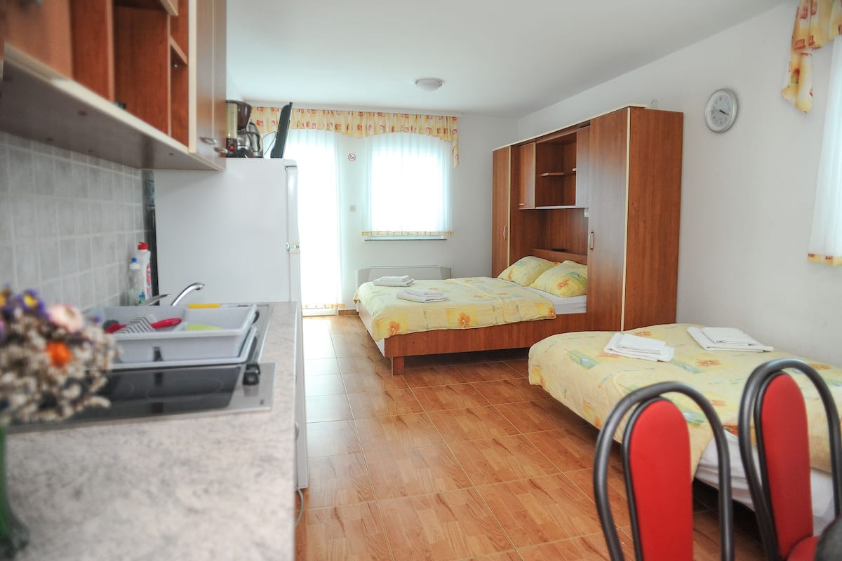 Ein kleines Zimmer mit Küchenzeile, zwei Betten und einem Holzschrank.