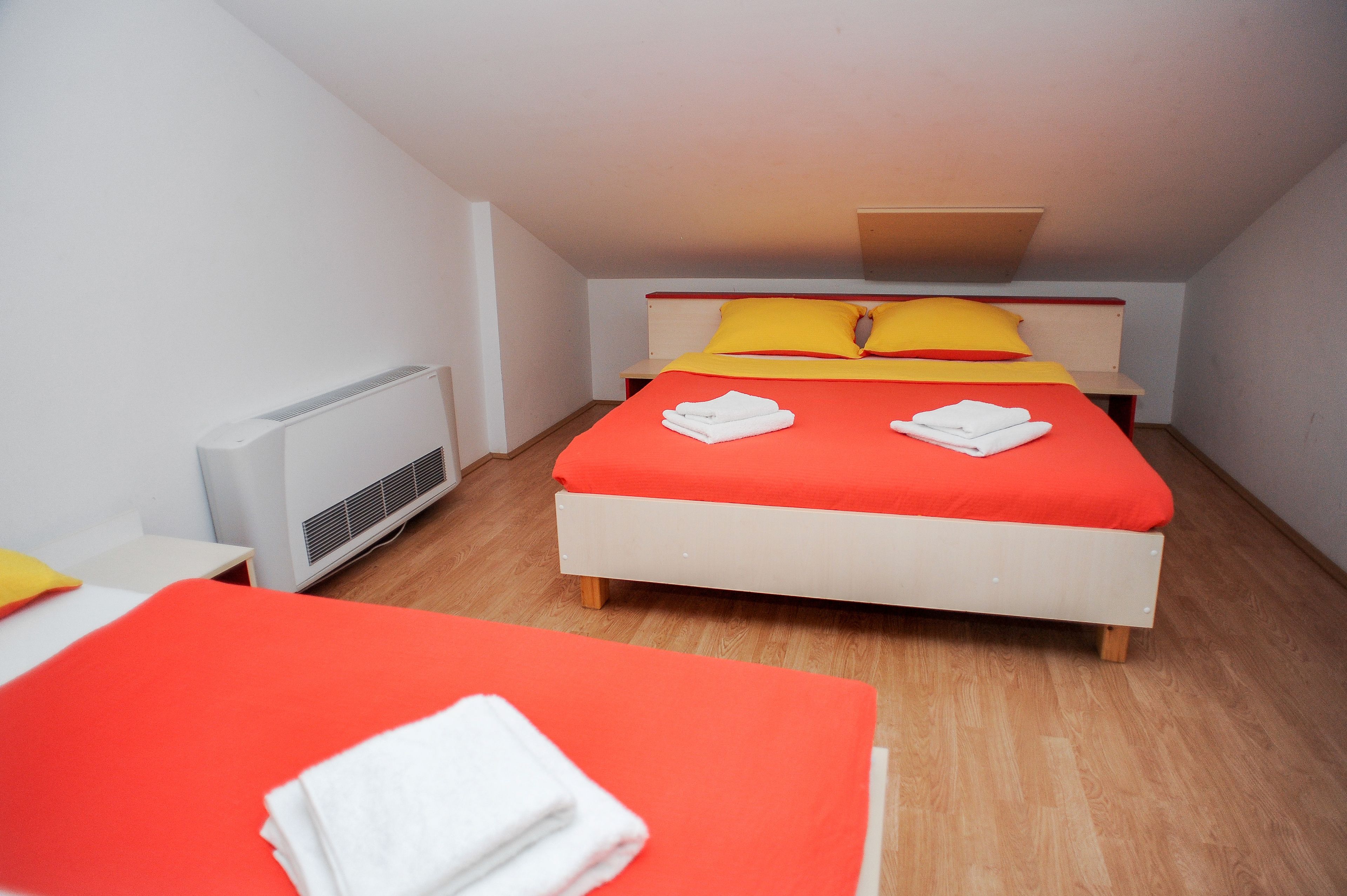 A single bed with red bedding and two pillows, a white bedside table, and a white radiator.