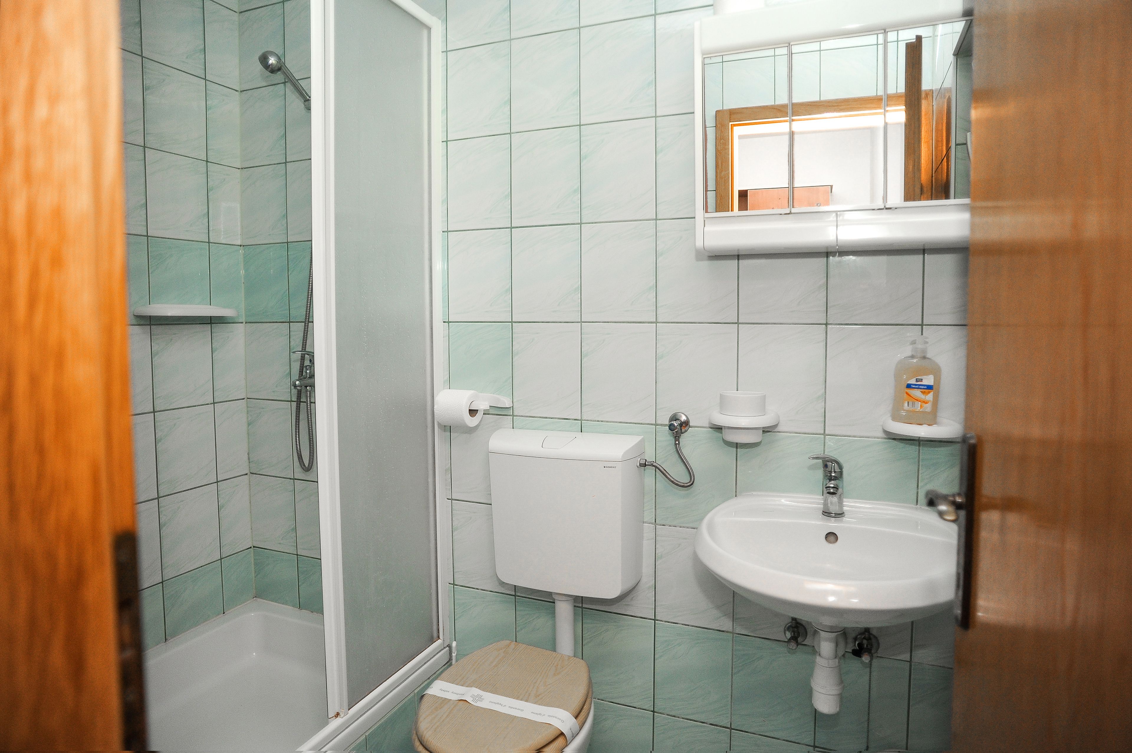 A bathroom with a shower, toilet, sink, and a mirror.