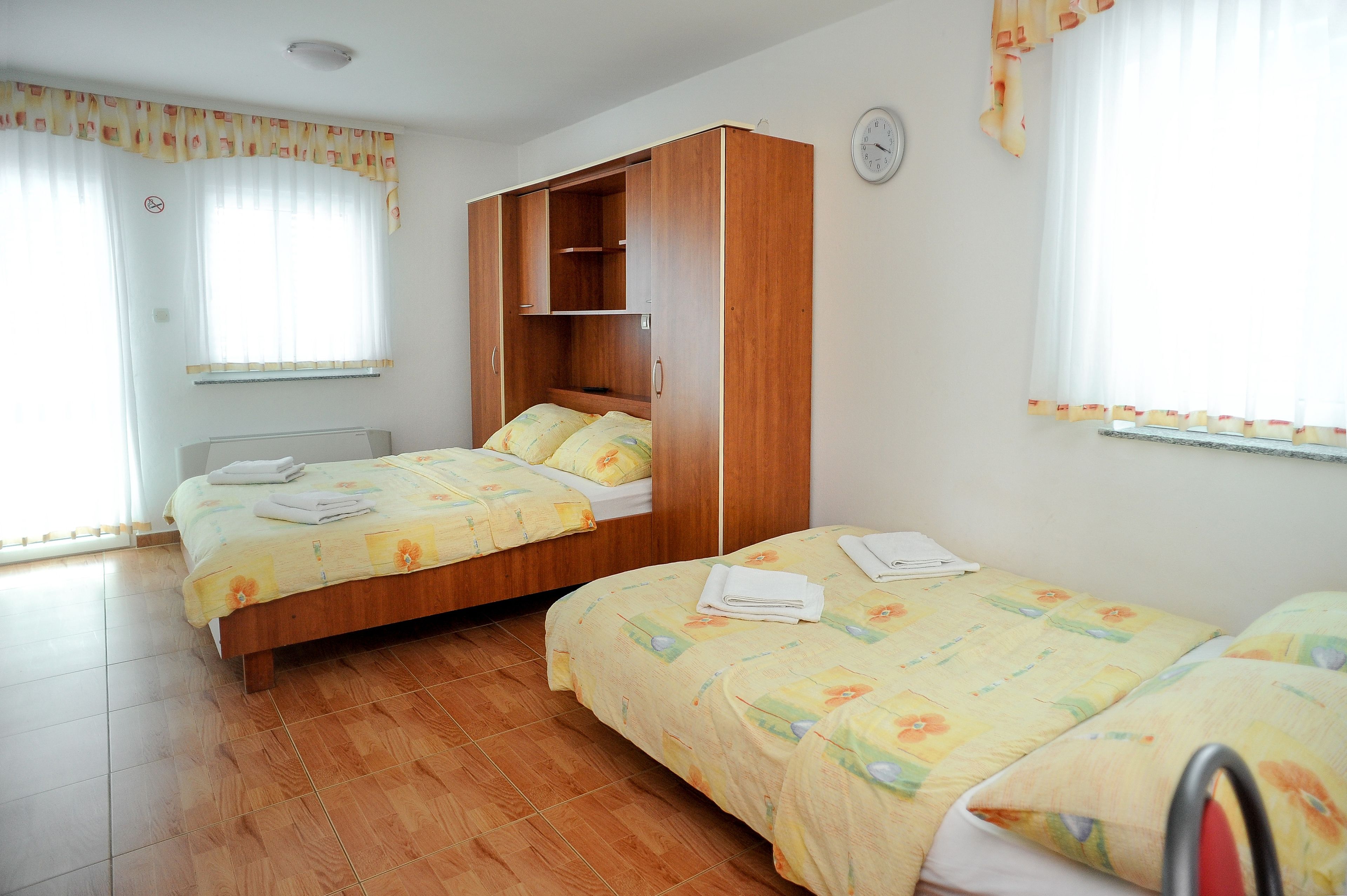 A bedroom with two beds, wooden wardrobe, and a clock on the wall.