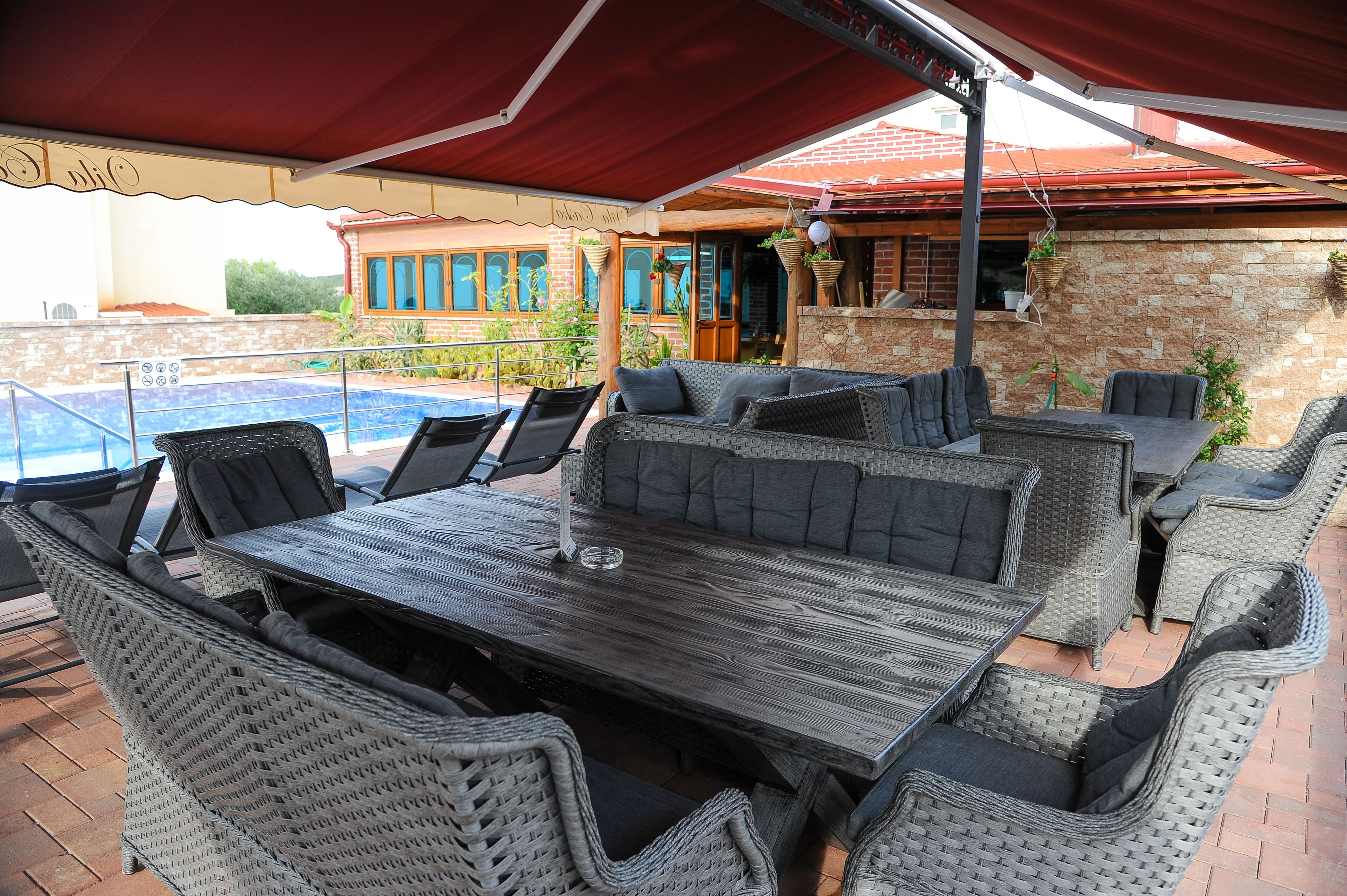 An outdoor patio with wicker furniture, a pool, and a brick building in the background.
