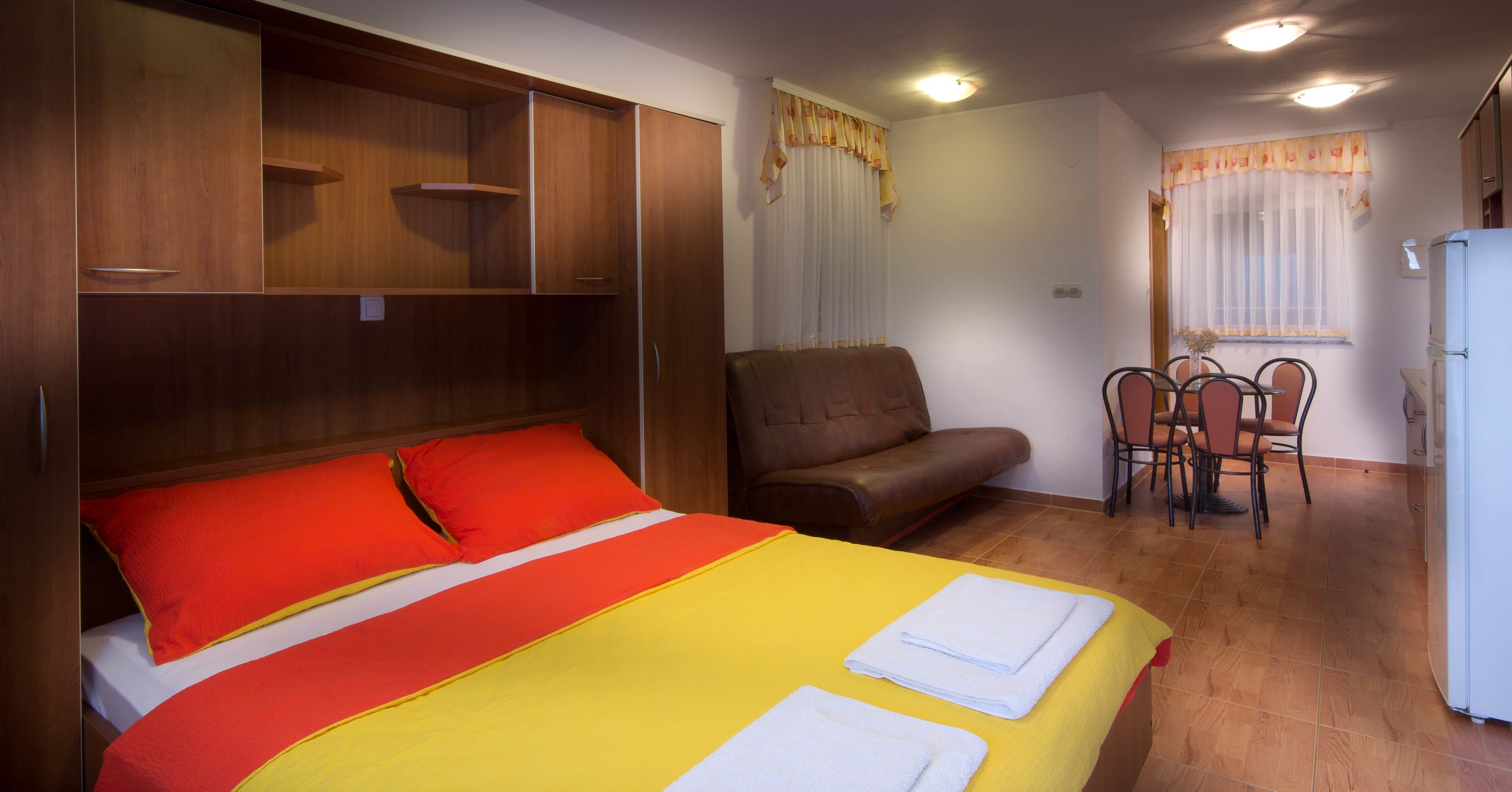 A hotel room with a bed, a sofa, a dining table with chairs, and a refrigerator.