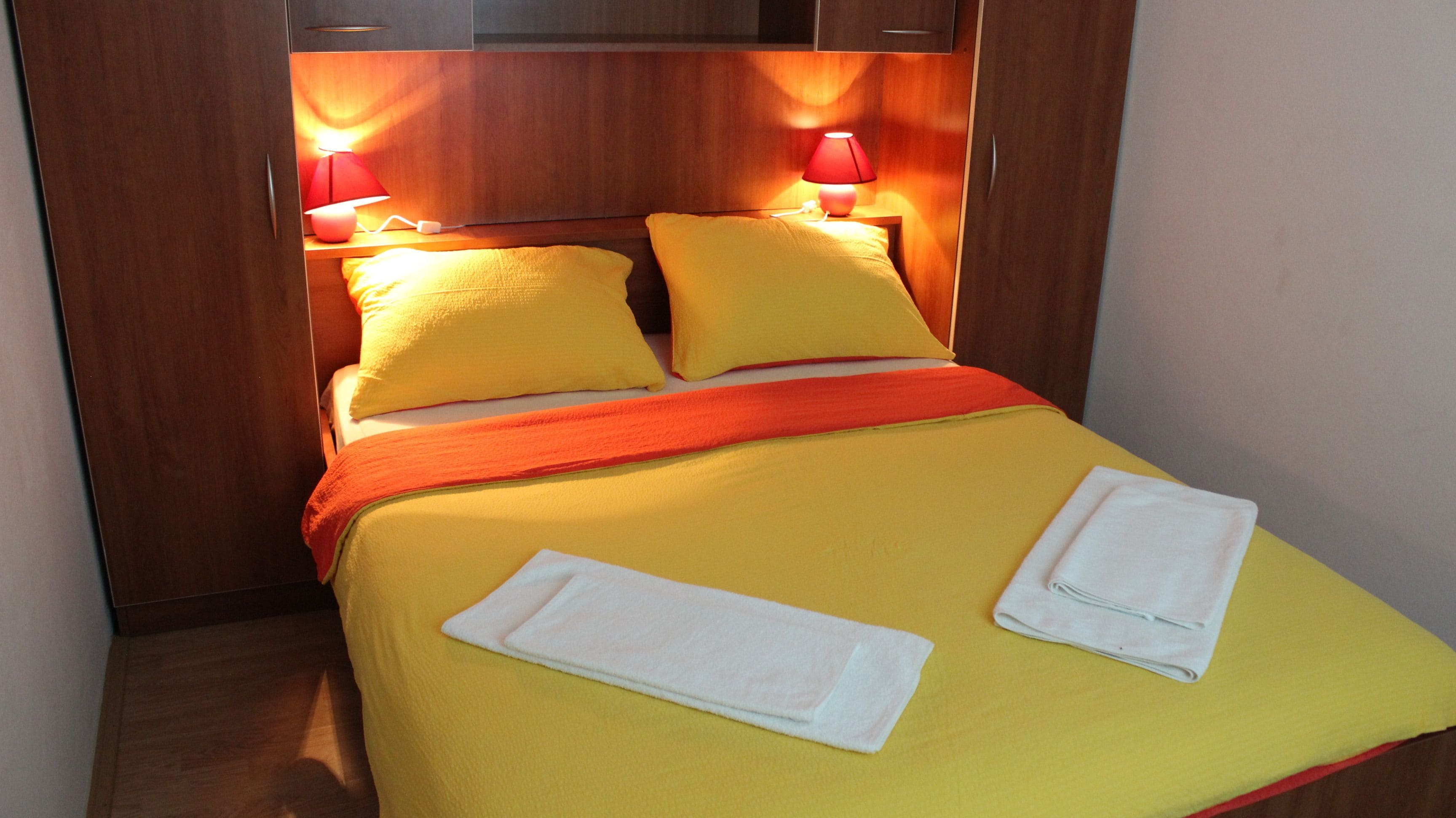 A neatly made bed with yellow bedding, two pillows, and two folded towels.