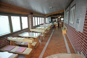 A long dining area with wooden tables and benches, brick walls, and large windows. - Vila Caska (Novalja)