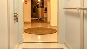 A hotel hallway with a round carpet, a mirror on the wall, and a door leading to a room with a bed and a desk. - BlueStone Boarding Apartments (Düsseldorf)