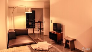 A modern hotel room with a sofa, a TV, a desk, and a staircase leading to an upper floor. - BlueStone Boarding Apartments (Düsseldorf)