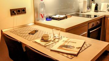 A hotel room with a small kitchenette, a welcome home booklet, a bottle of water, a glass, and a cup on the counter.