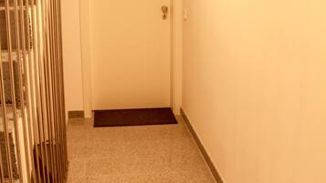 Um corredor estreito com uma porta branca no final, um corrimão de metal à esquerda e piso coberto de carpete.