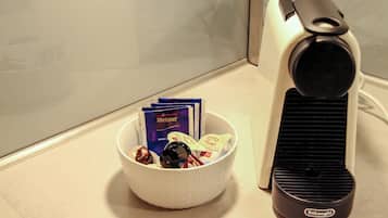 A white bowl containing various items including a bottle, a pack of Meijer chocolate, and some cards, placed next to a black and white coffee maker on a tiled surface.